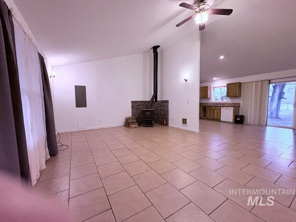 Unfurnished living room featuring a wood stove, light tile patterned floors, electric panel, ceiling fan, and high vaulted ceiling