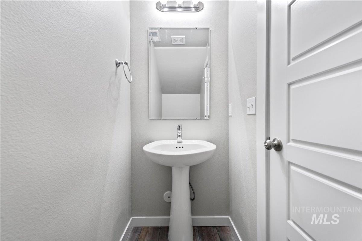 Half bath with a textured wall and dark wood-style flooring