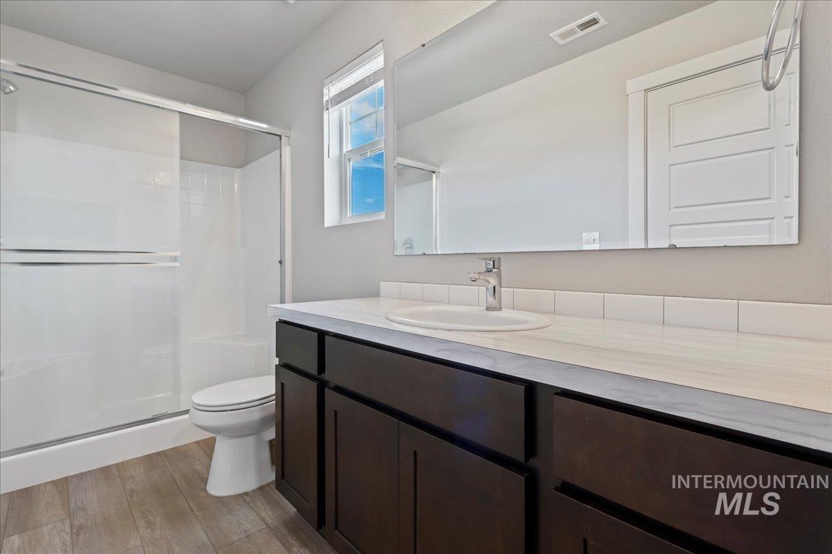 Full bath with light wood-style floors, vanity, and a stall shower