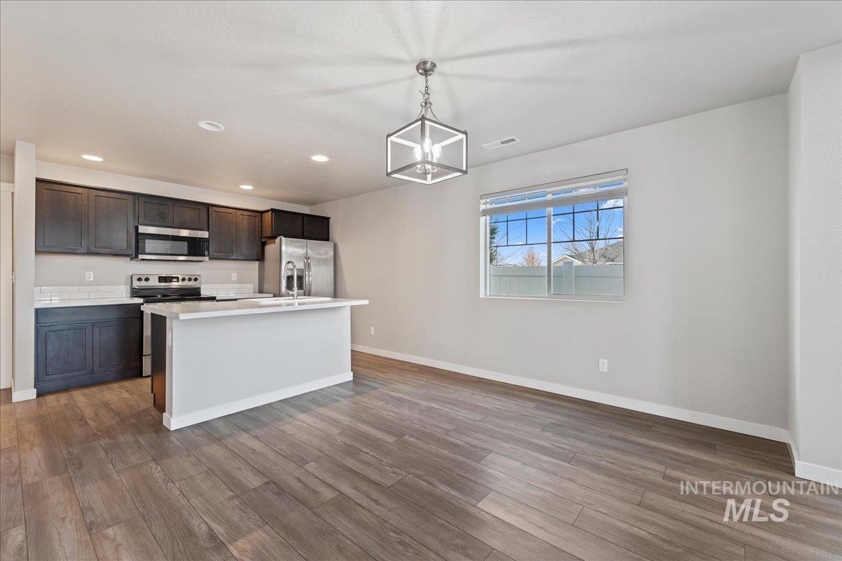 Kitchen with stainless steel appliances, light countertops, pendant lighting, a kitchen island with sink, and light wood finished floors