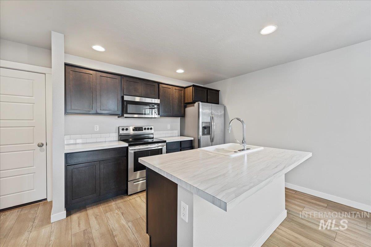 Kitchen with appliances with stainless steel finishes, light countertops, dark brown cabinets, a kitchen island with sink, and recessed lighting