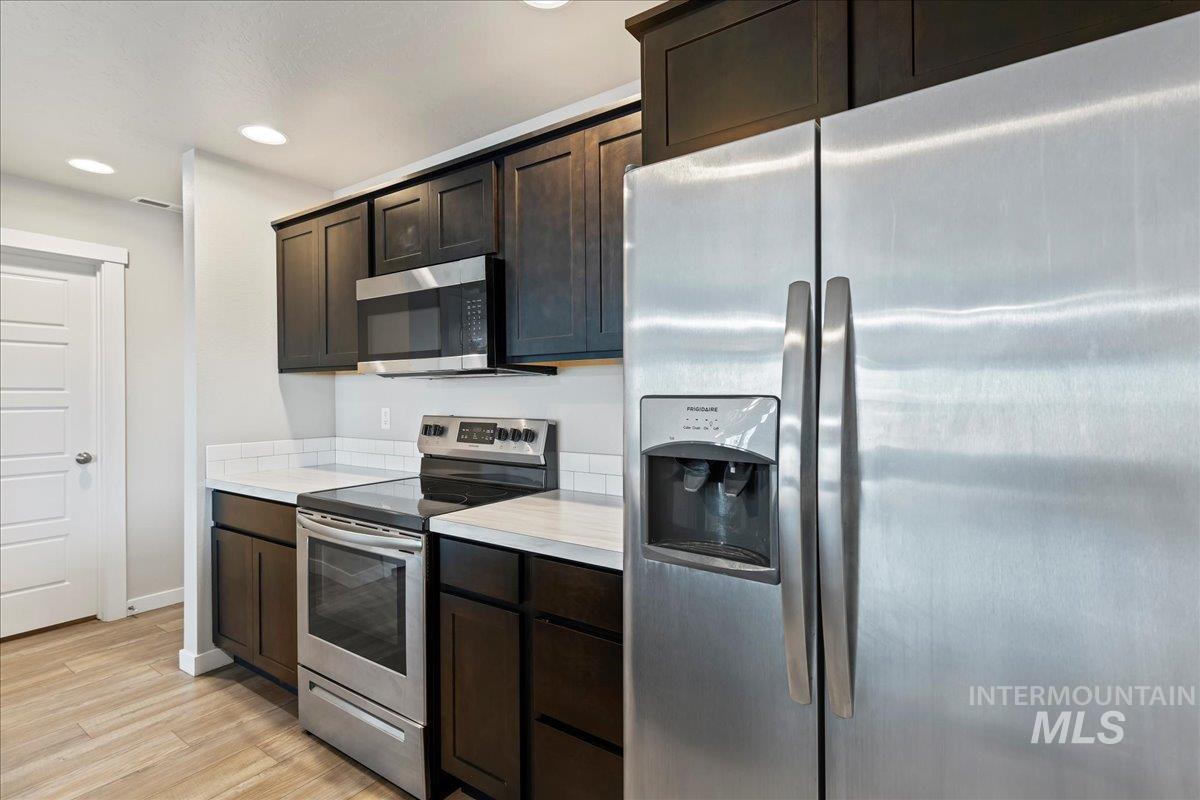 Kitchen with stainless steel appliances, light countertops, dark brown cabinets, recessed lighting, and light wood finished floors