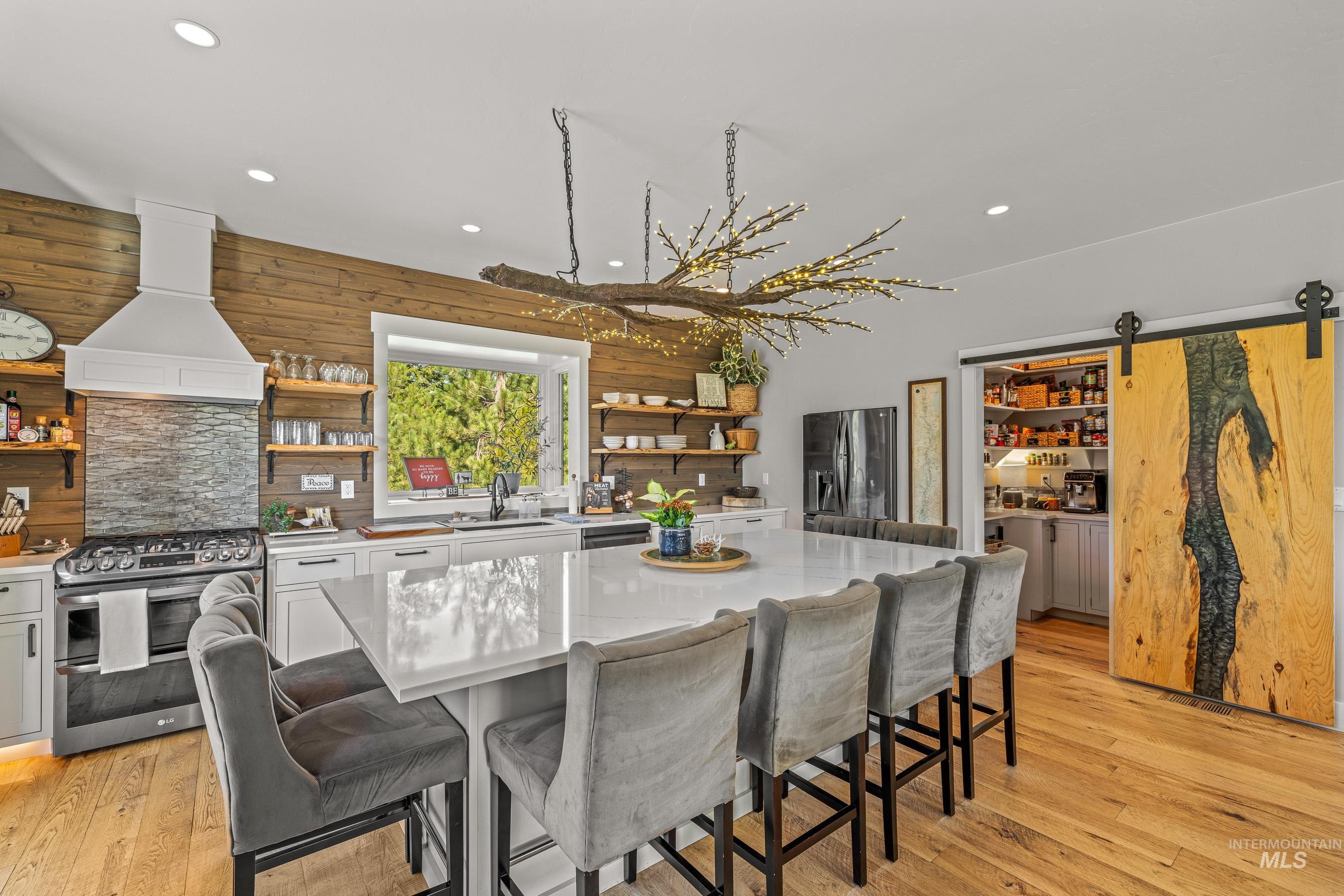 Kitchen featuring a barn door, appliances with stainless steel finishes, custom range hood, open shelves, and a breakfast bar