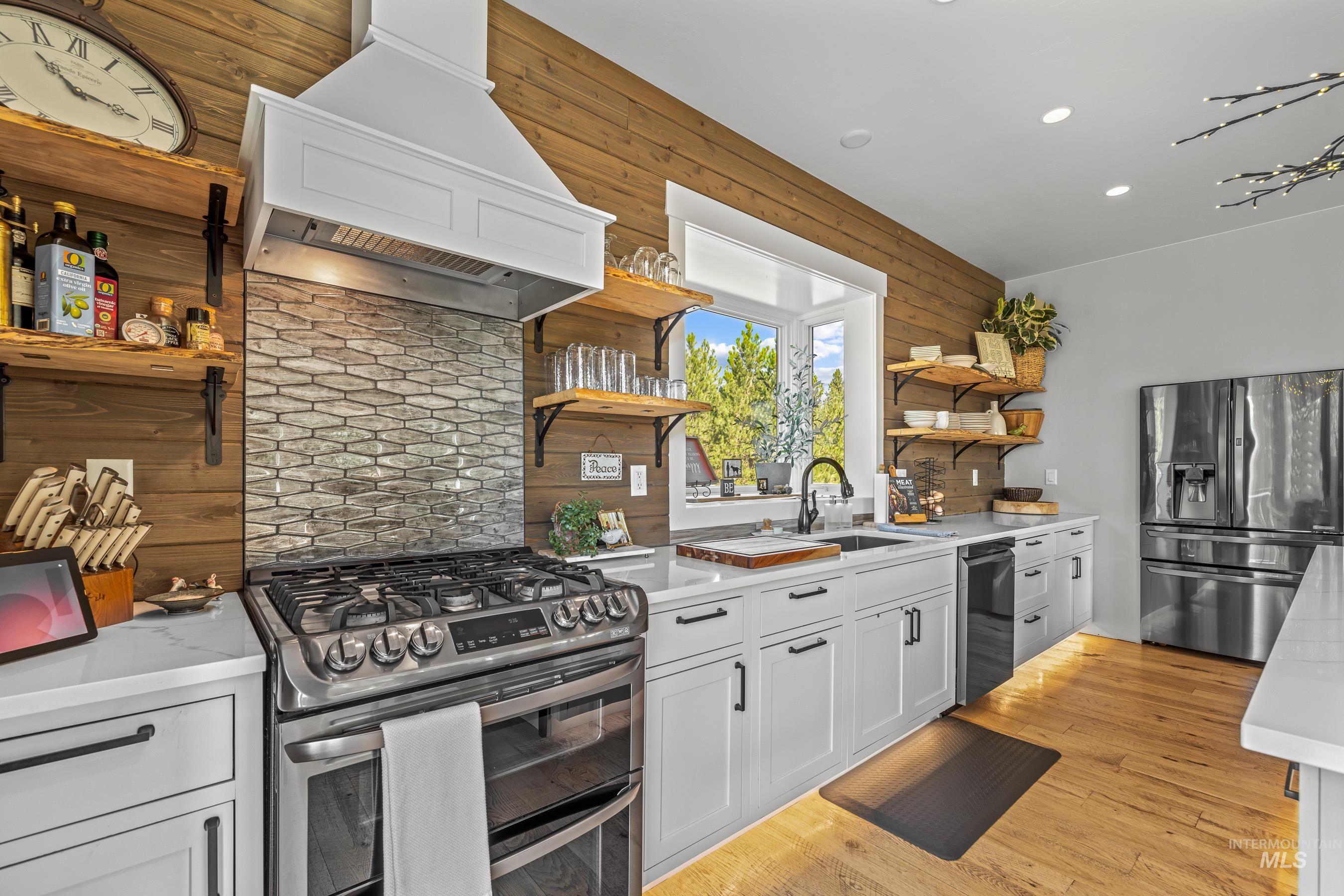 Kitchen with open shelves, white cabinets, stainless steel appliances, custom exhaust hood, and light wood-style floors
