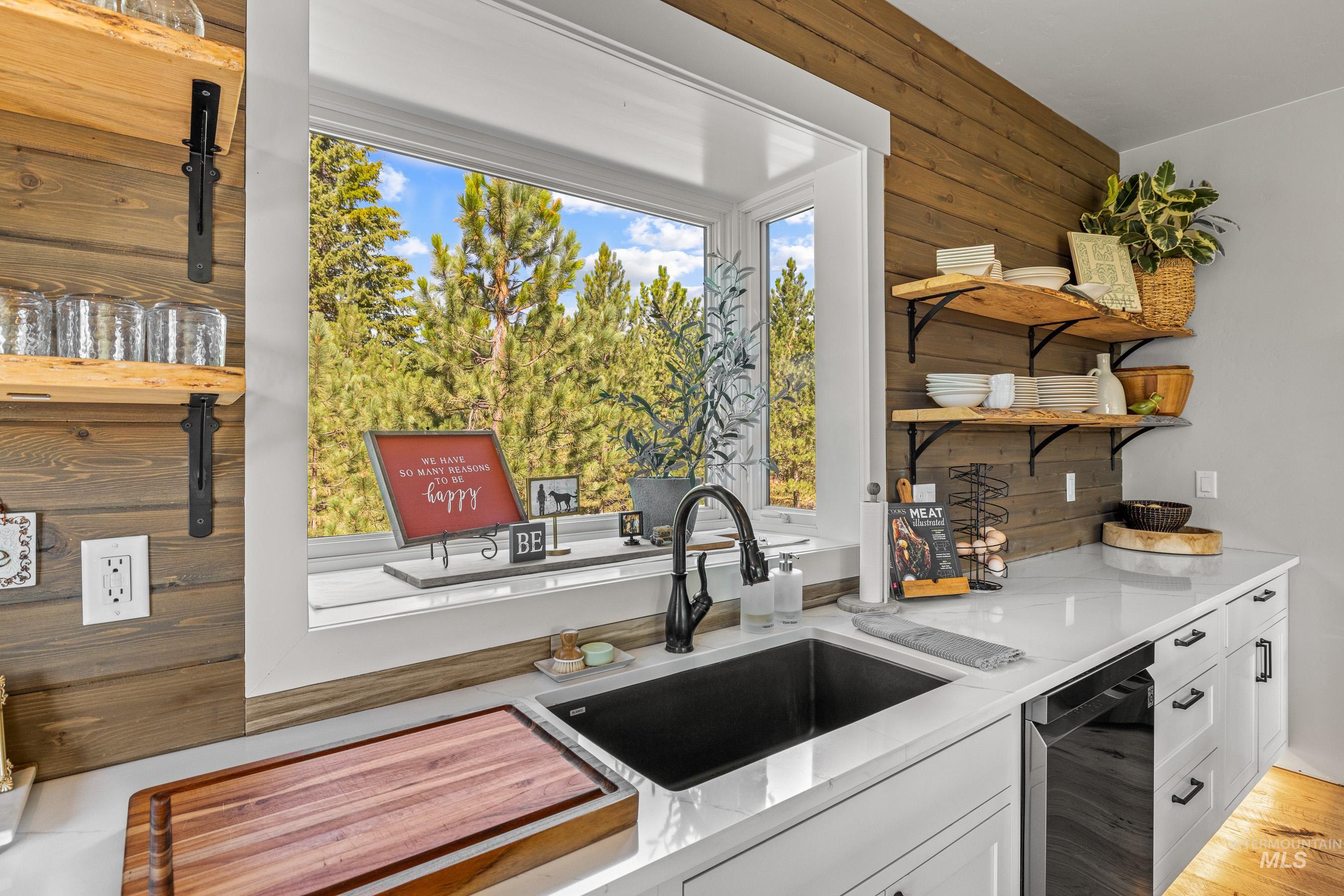 Kitchen featuring white cabinetry, open shelves, light stone counters, dishwasher, and wooden walls