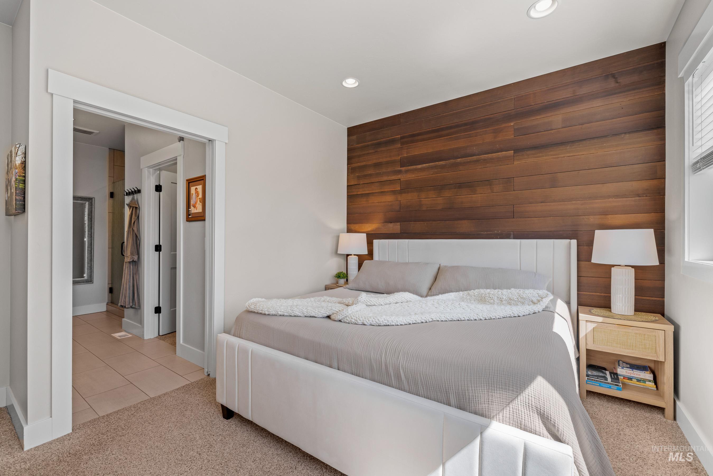 Bedroom featuring an accent wall, wood walls, light colored carpet, and ensuite bath