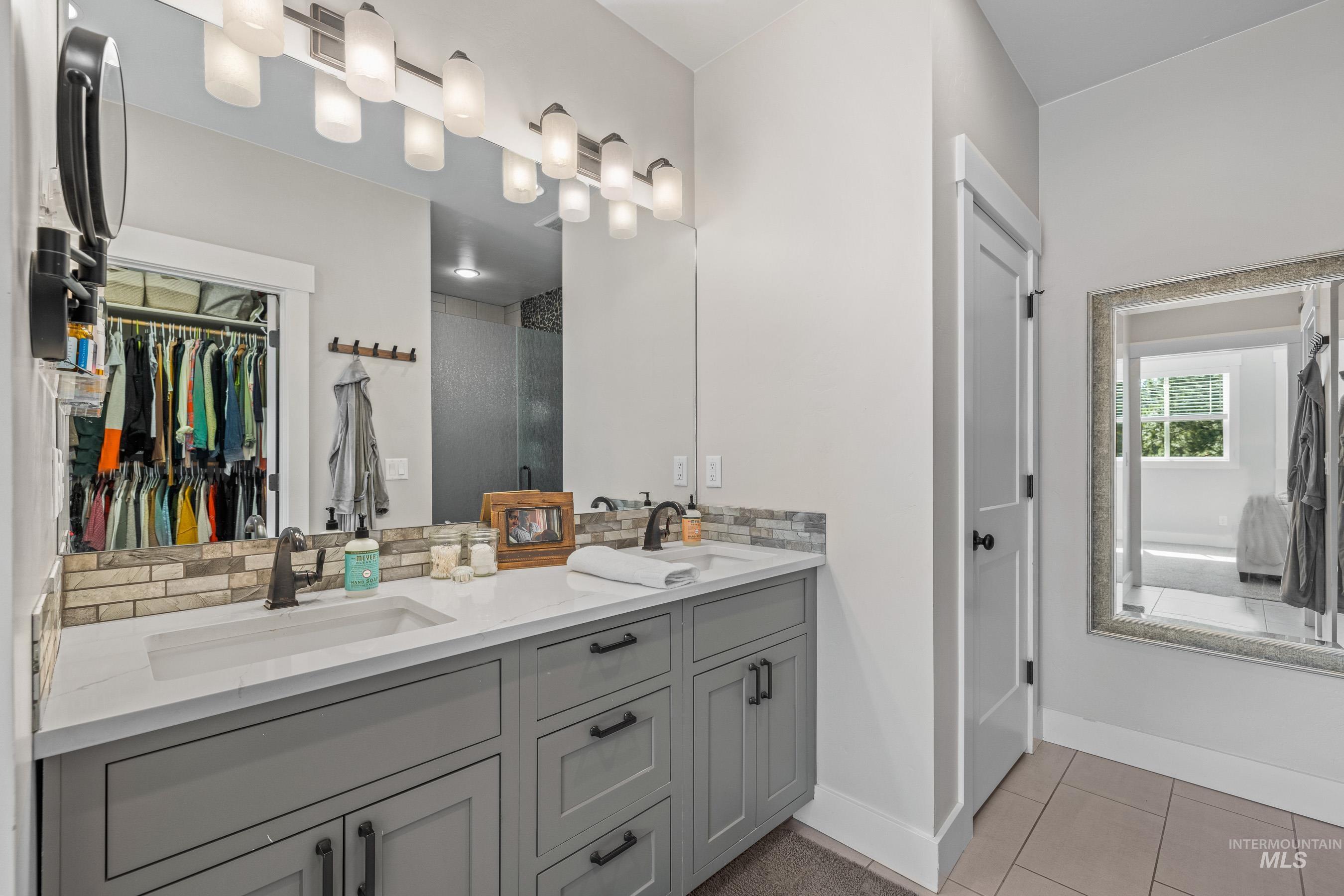 Bathroom with a spacious closet, light tile patterned floors, double vanity, and a stall shower
