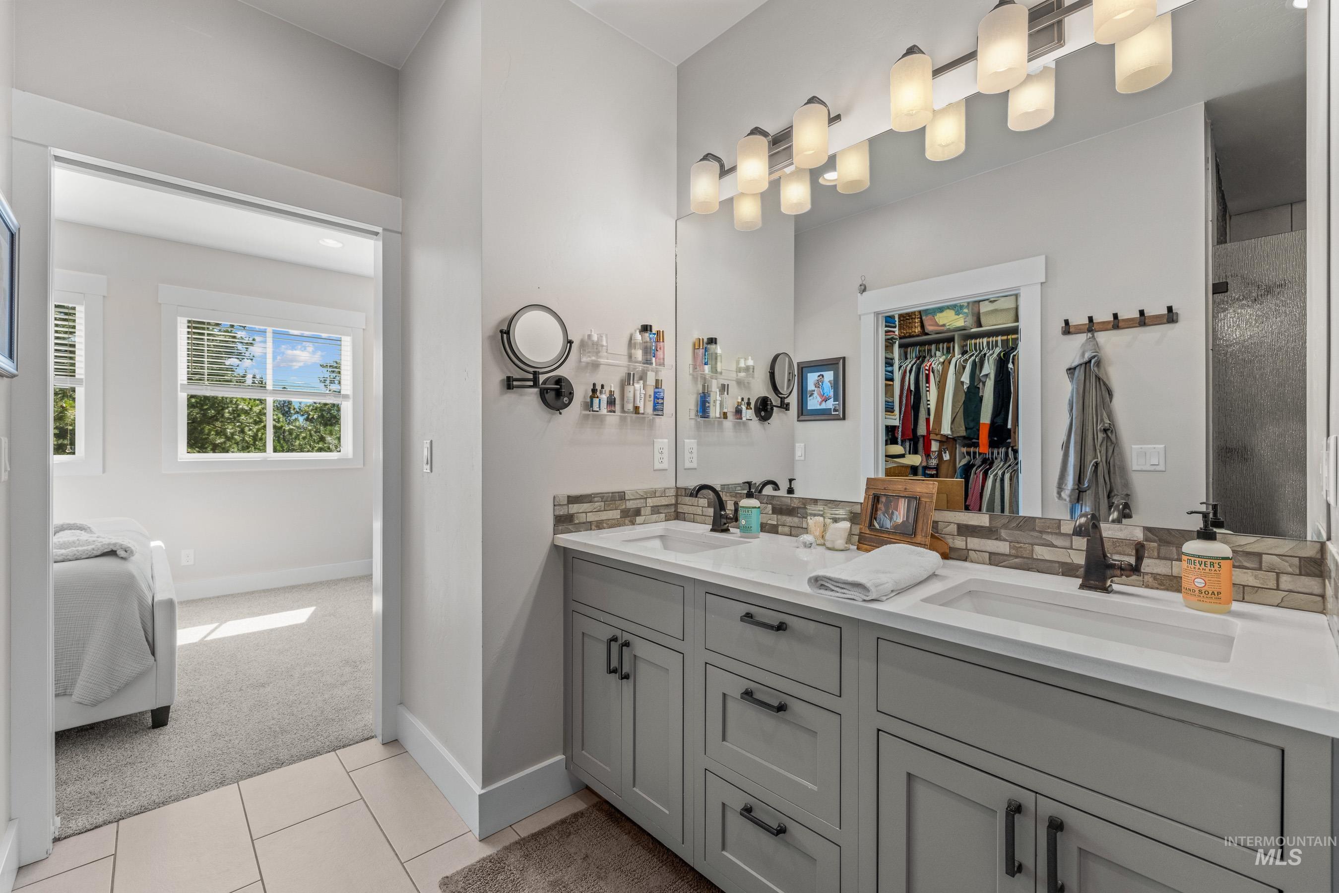Ensuite bathroom featuring light carpet, double vanity, a walk in closet, and light tile patterned flooring