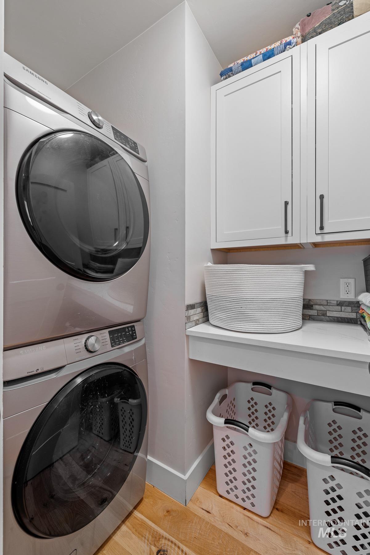 Washroom featuring cabinet space, light wood-style flooring, and stacked washer and clothes dryer