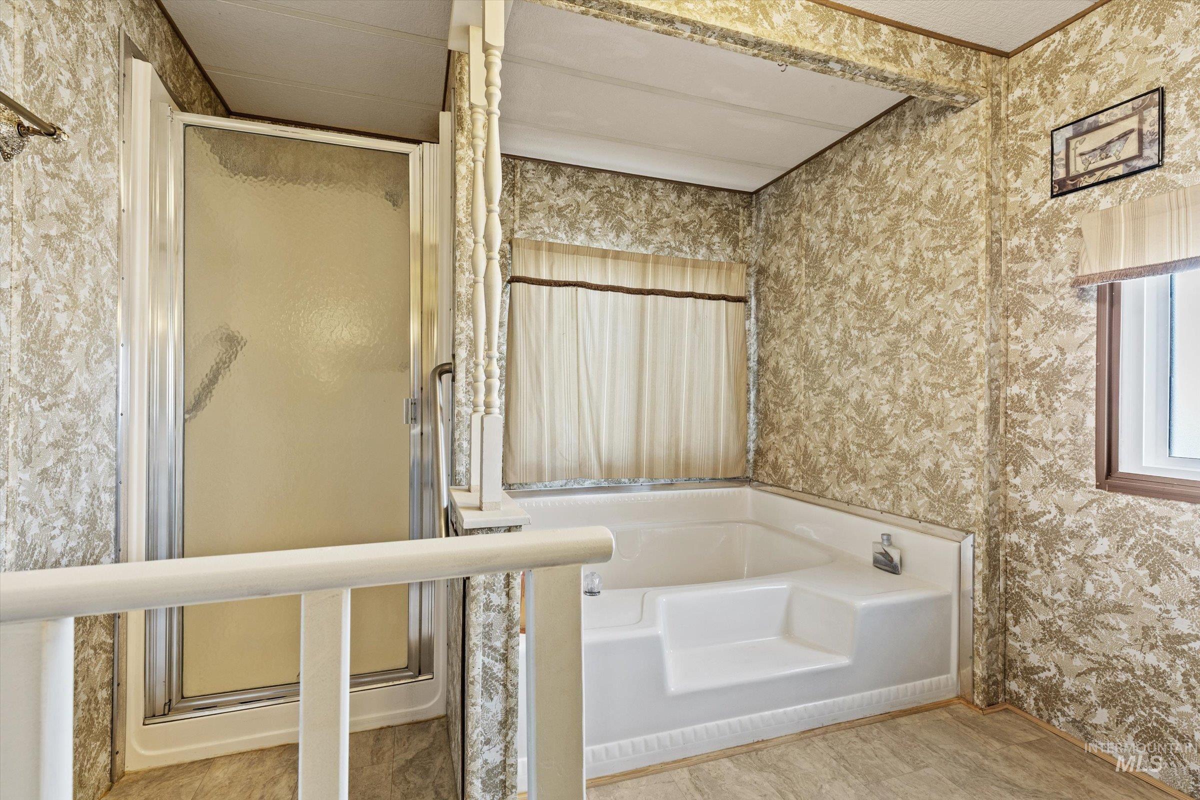 Bathroom featuring wallpapered walls, a bath, and a stall shower