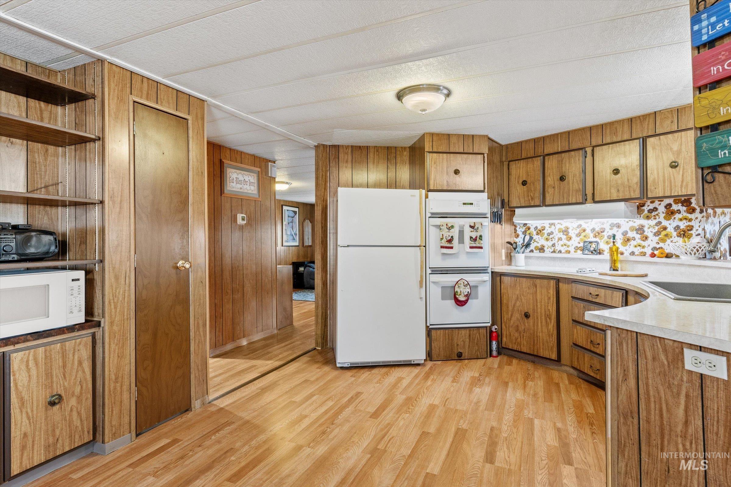 Kitchen with open shelves, brown cabinets, white appliances, light countertops, and light wood-style flooring