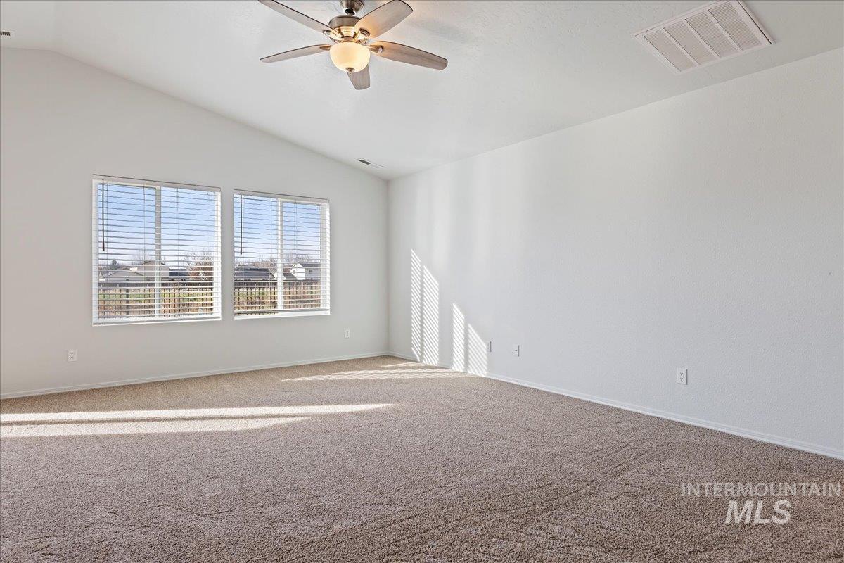 Carpeted spare room with vaulted ceiling and a ceiling fan