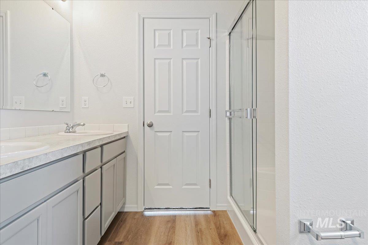 Full bath featuring double vanity, light wood-type flooring, a stall shower, and a textured wall