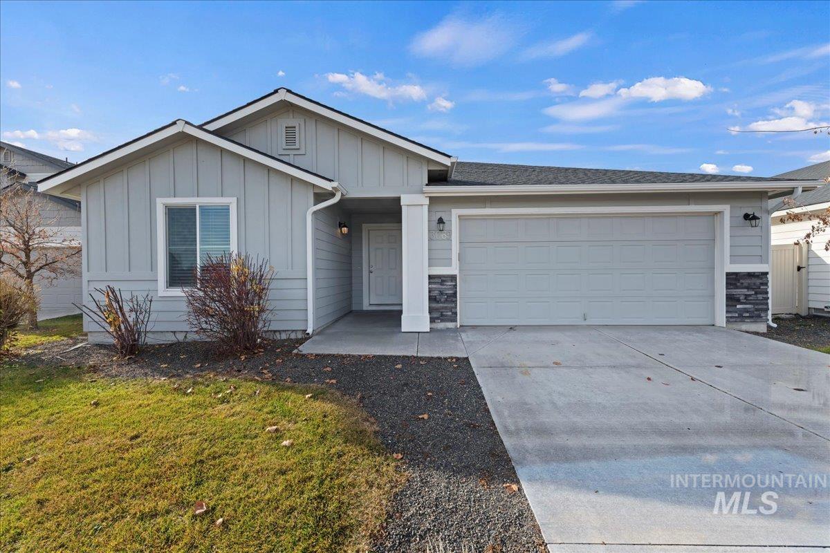 View of front of property with board and batten siding, stone siding, driveway, an attached garage, and a front yard