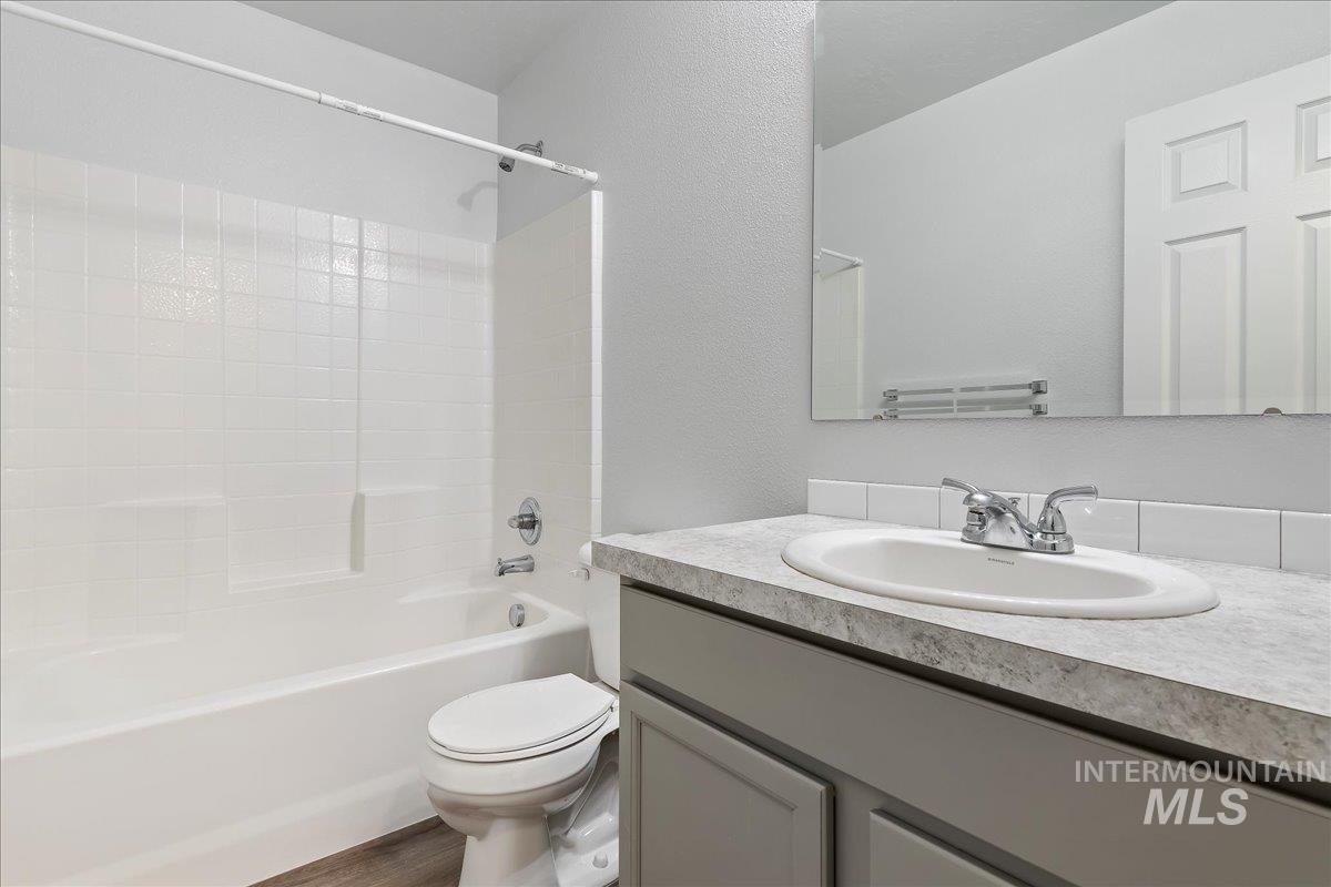 Bathroom with shower / bathtub combination, vanity, a textured wall, and wood finished floors