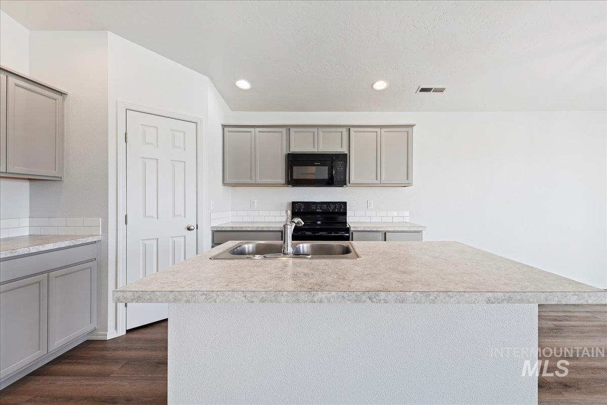 Kitchen with gray cabinets, light countertops, black appliances, a center island with sink, and recessed lighting