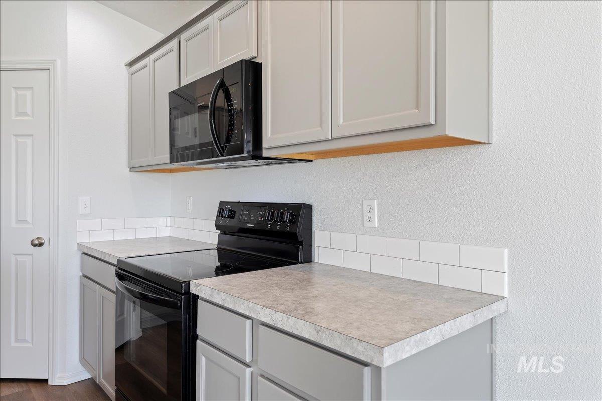 Kitchen featuring black appliances, light countertops, gray cabinetry, and dark wood-style floors