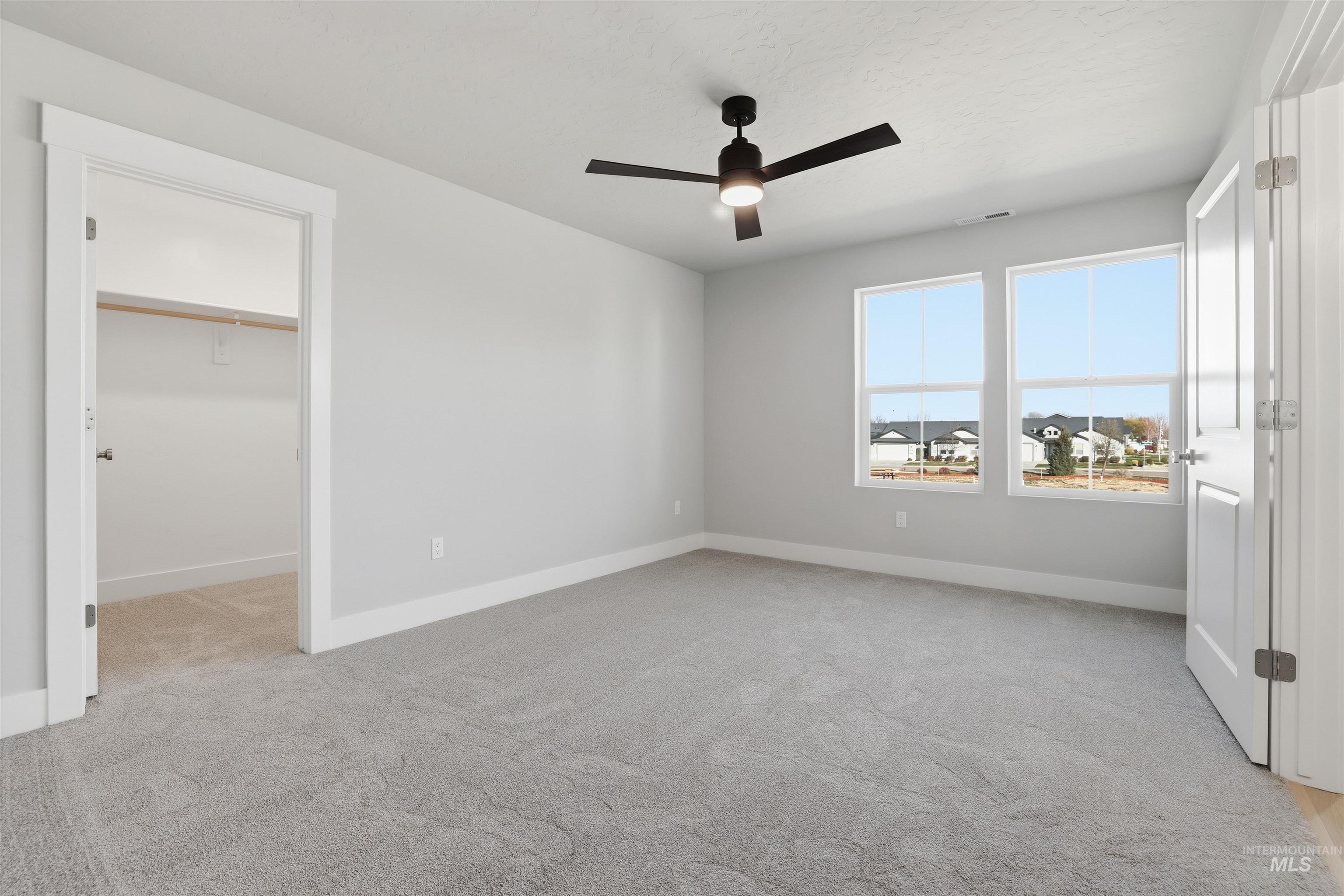 Unfurnished bedroom featuring a spacious closet, ceiling fan, and light colored carpet
