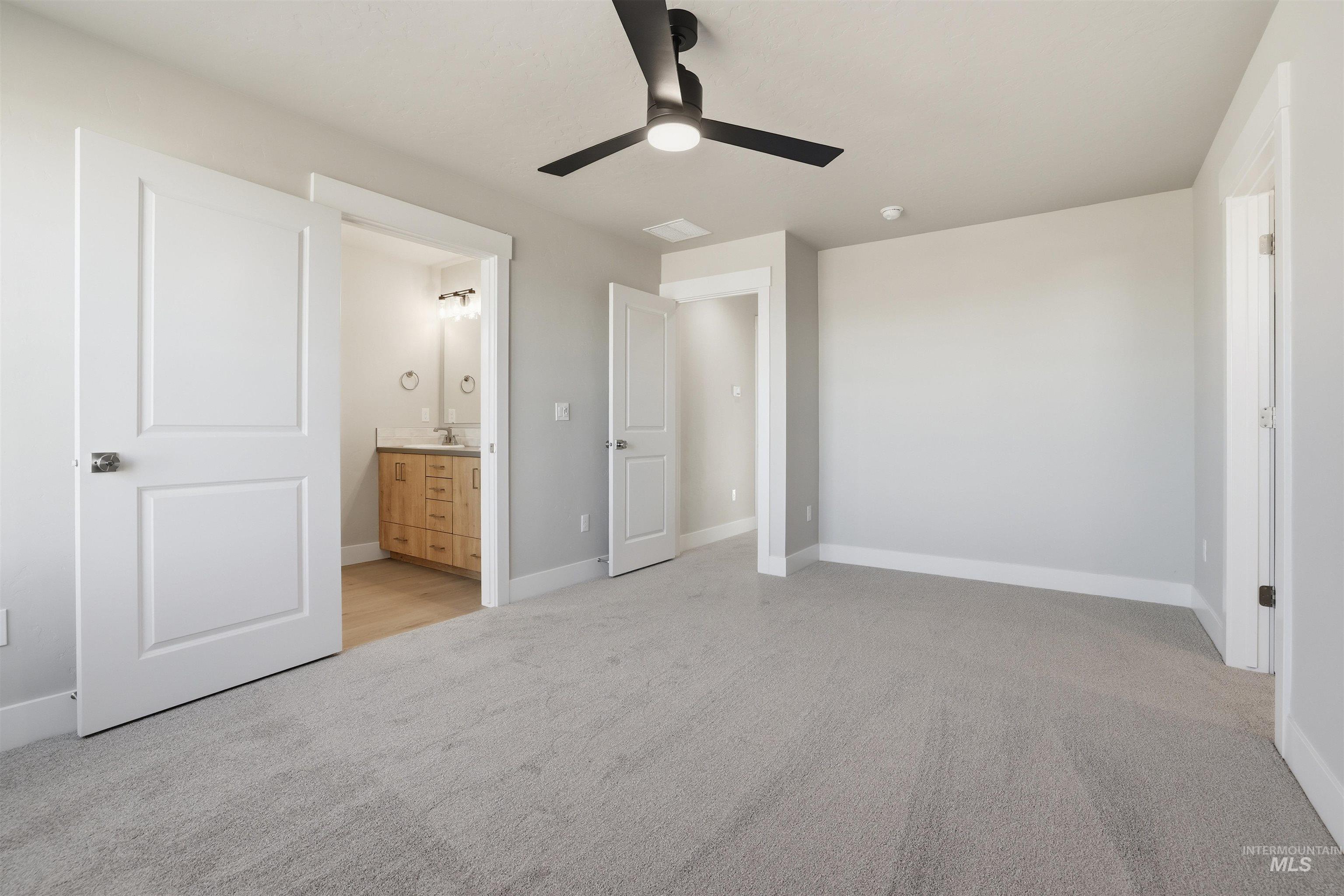 Unfurnished bedroom featuring light carpet, a ceiling fan, and ensuite bath
