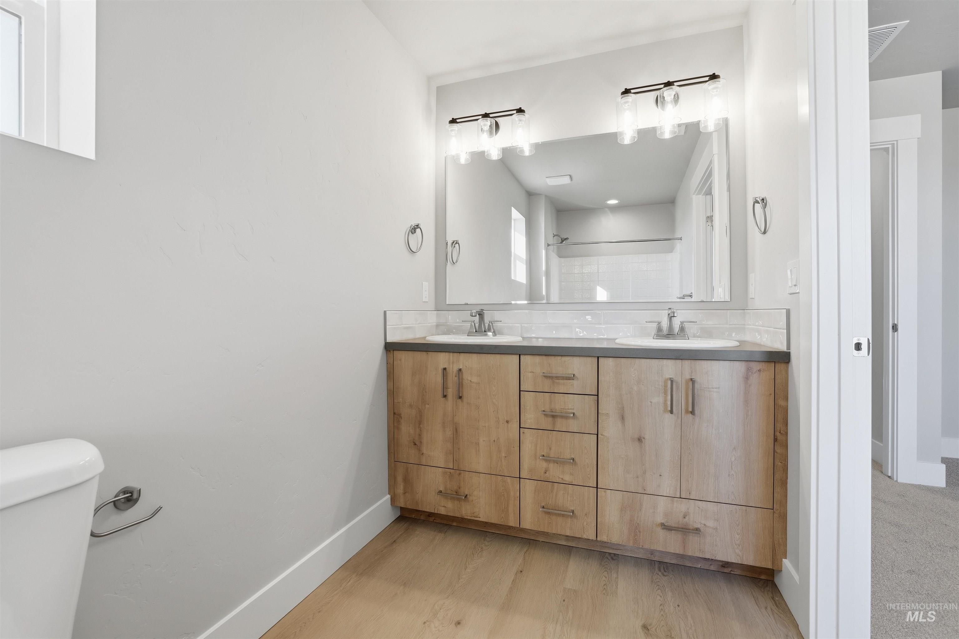 Full bath featuring double vanity, light wood finished floors, and a shower