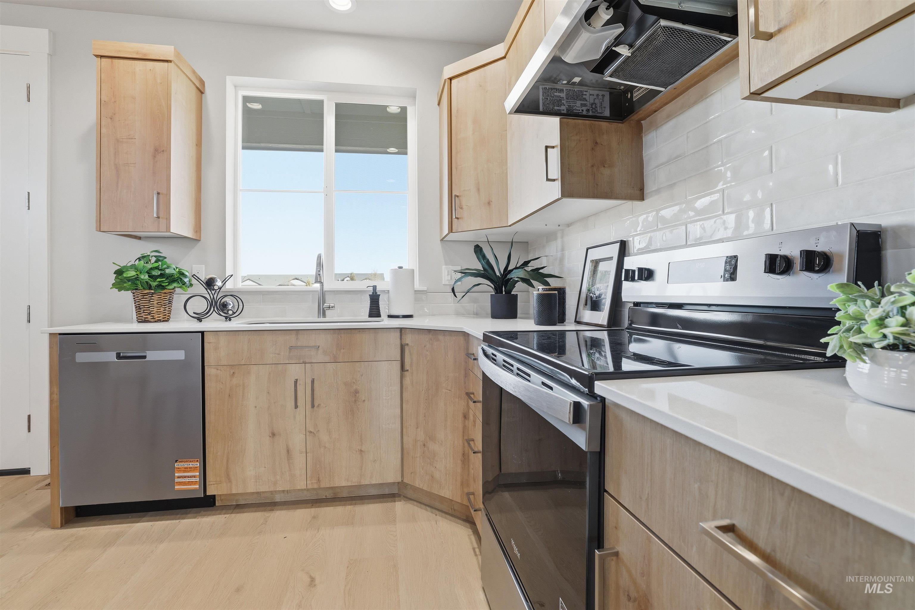Kitchen with light brown cabinets, stainless steel appliances, extractor fan, light stone countertops, and light wood-style flooring