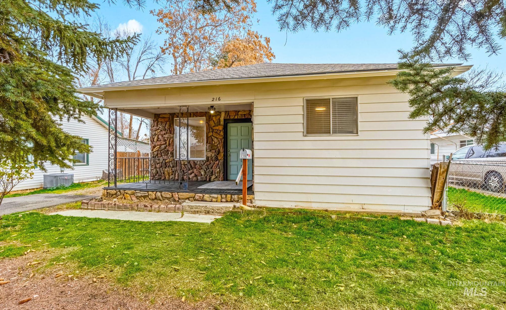 Ranch-style home featuring covered porch, a shingled roof, and stone siding