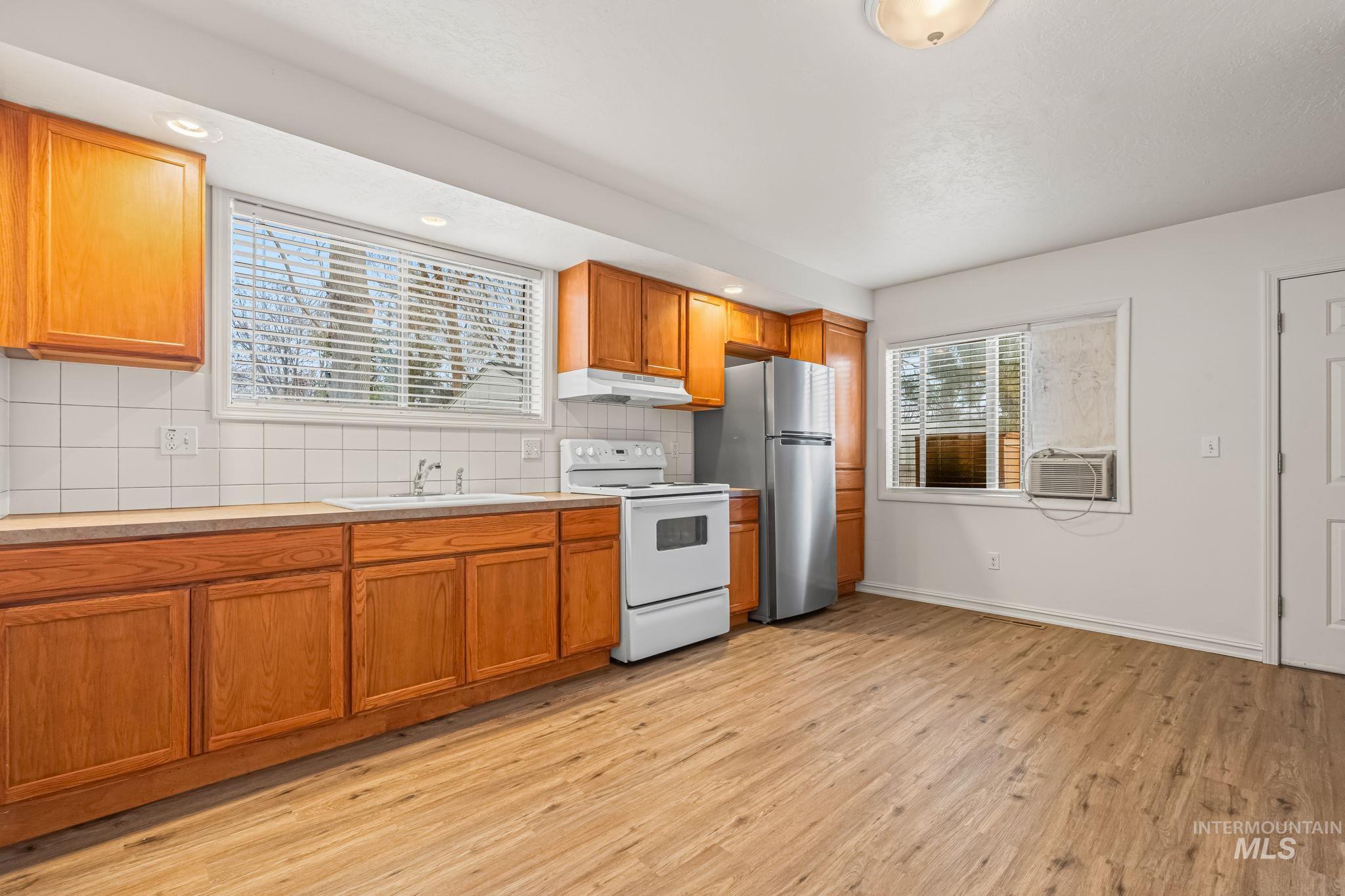 Kitchen featuring decorative backsplash, electric stove, brown cabinets, freestanding refrigerator, and light wood-style floors