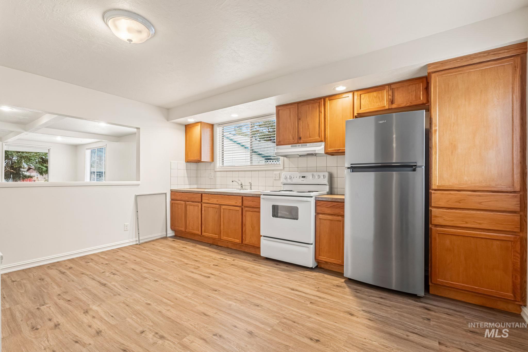 Kitchen with freestanding refrigerator, white electric range, light countertops, light wood-style flooring, and decorative backsplash
