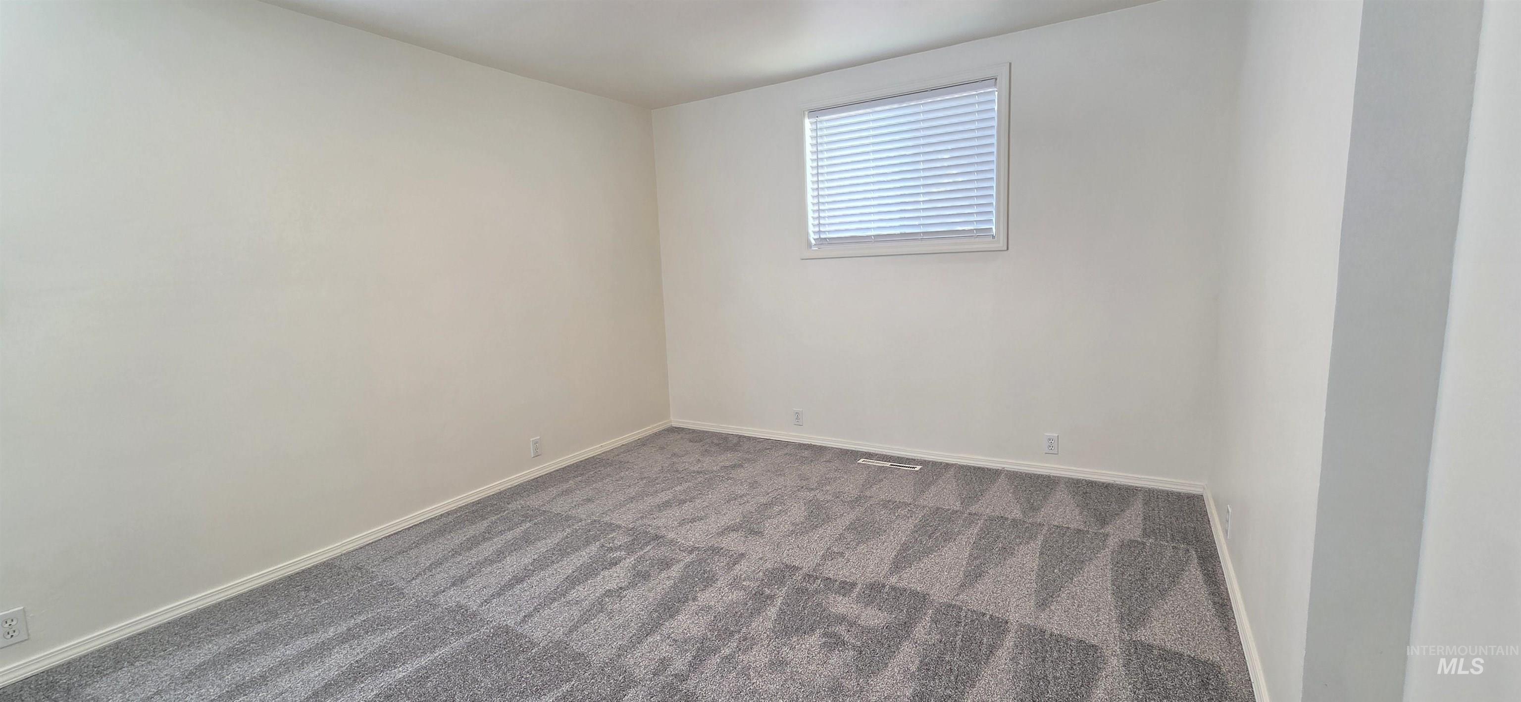 Empty room featuring dark colored carpet and baseboards