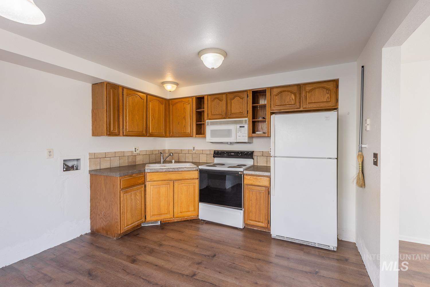 Kitchen featuring white appliances, brown cabinets, dark countertops, dark wood-style flooring, and open shelves