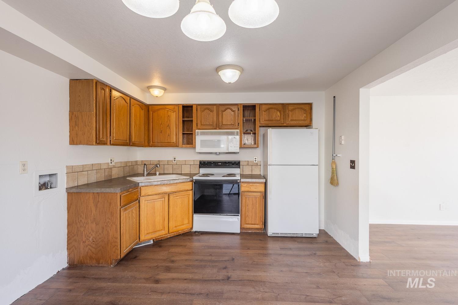 Kitchen featuring white appliances, brown cabinets, and dark wood-style floors
