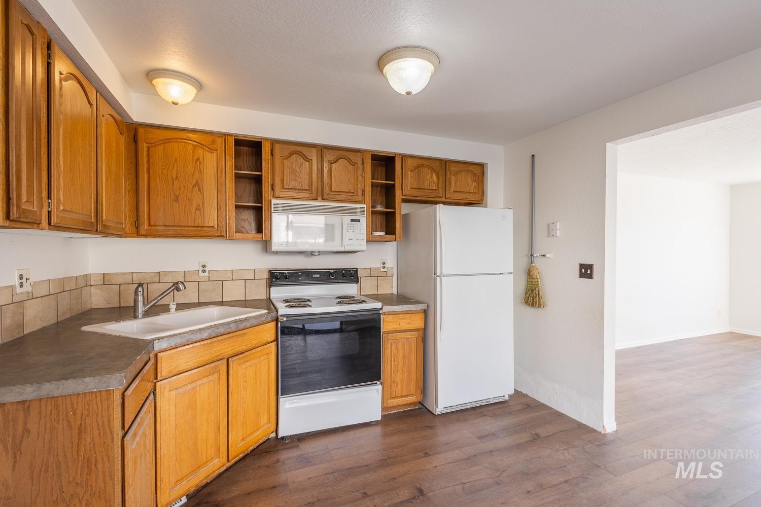 Kitchen featuring white appliances, brown cabinets, dark wood-style flooring, dark countertops, and open shelves