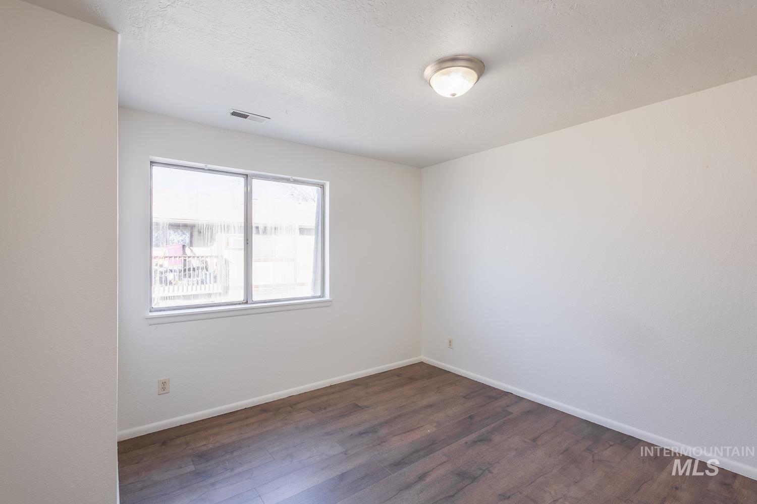 Unfurnished room featuring dark wood-style flooring and a textured ceiling
