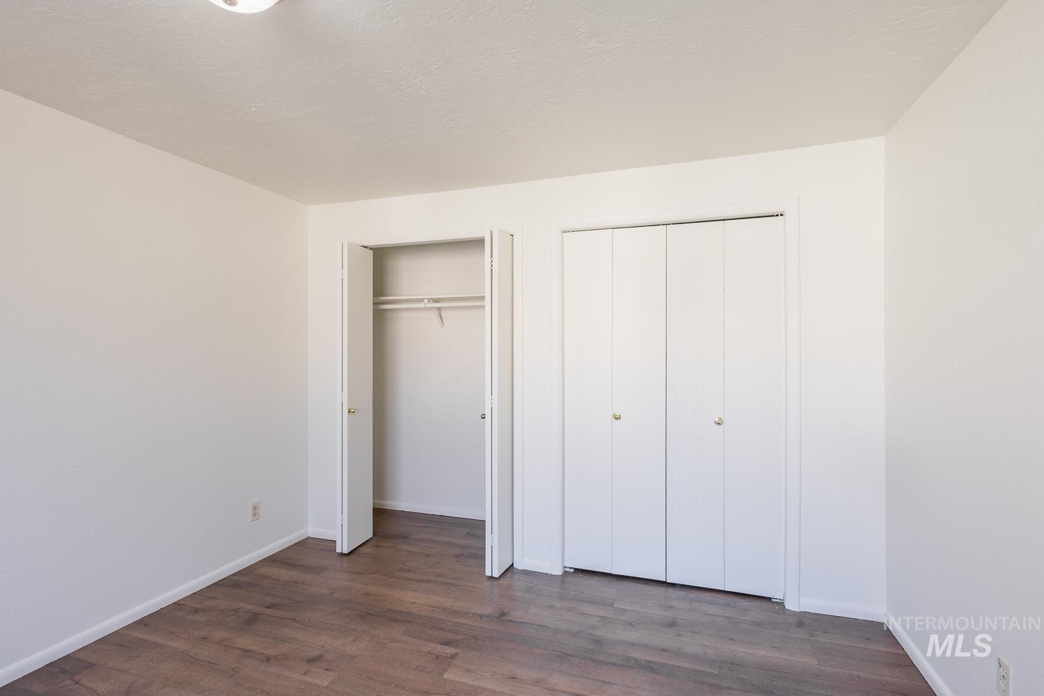 Unfurnished bedroom with multiple closets, dark wood finished floors, and a textured ceiling