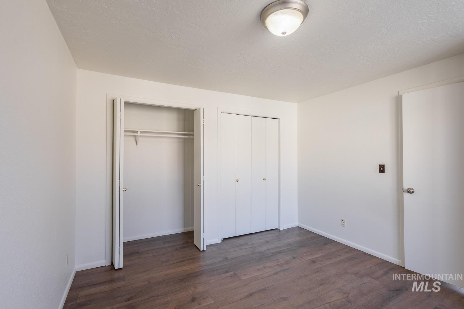 Unfurnished bedroom with multiple closets, dark wood-style floors, and a textured ceiling