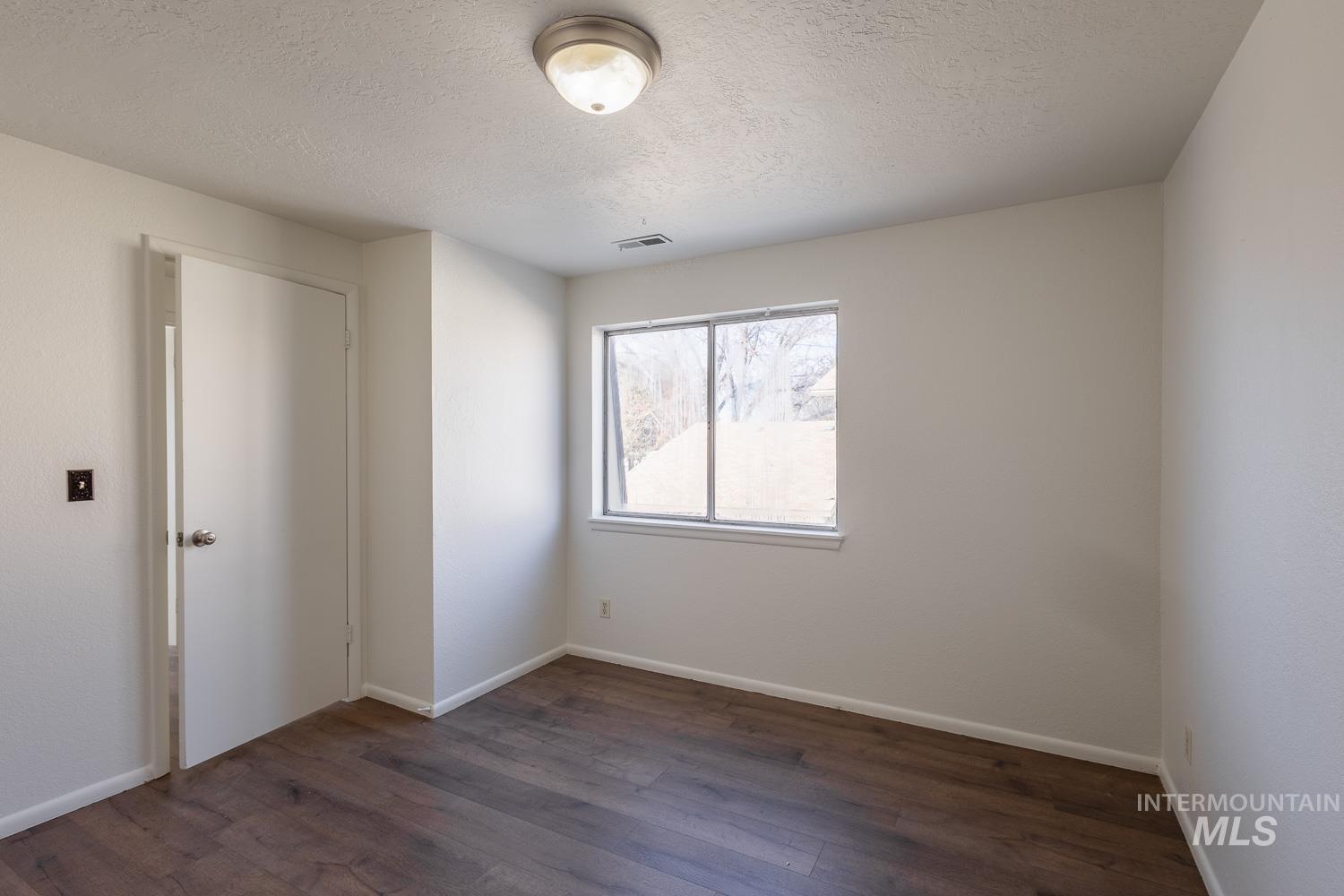 Empty room with a textured ceiling and dark wood-type flooring