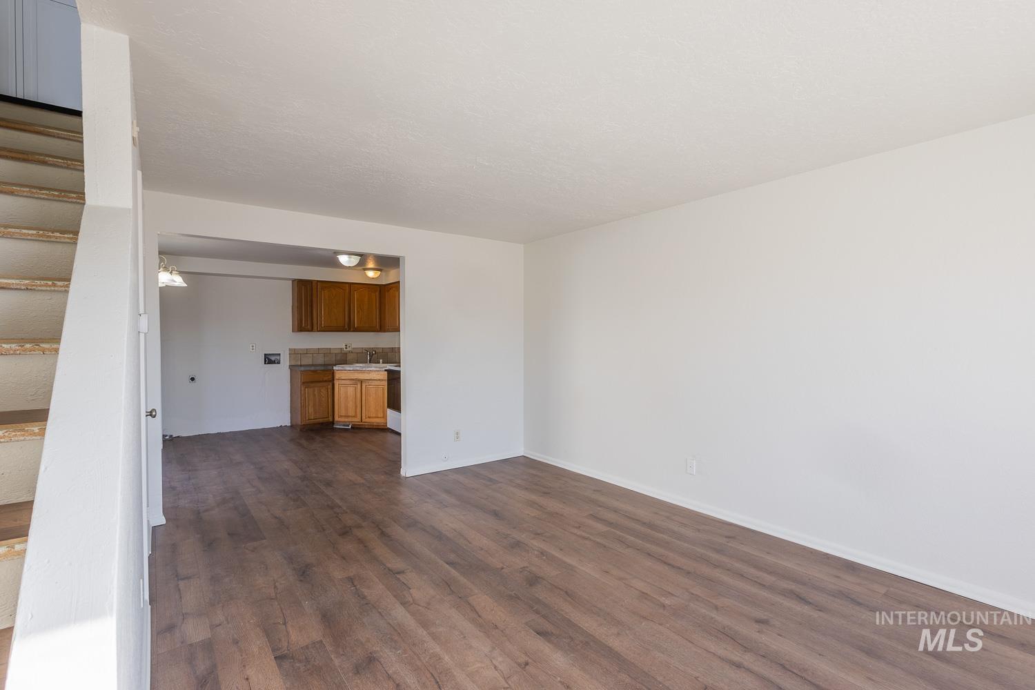 Unfurnished living room featuring dark wood-type flooring and stairway