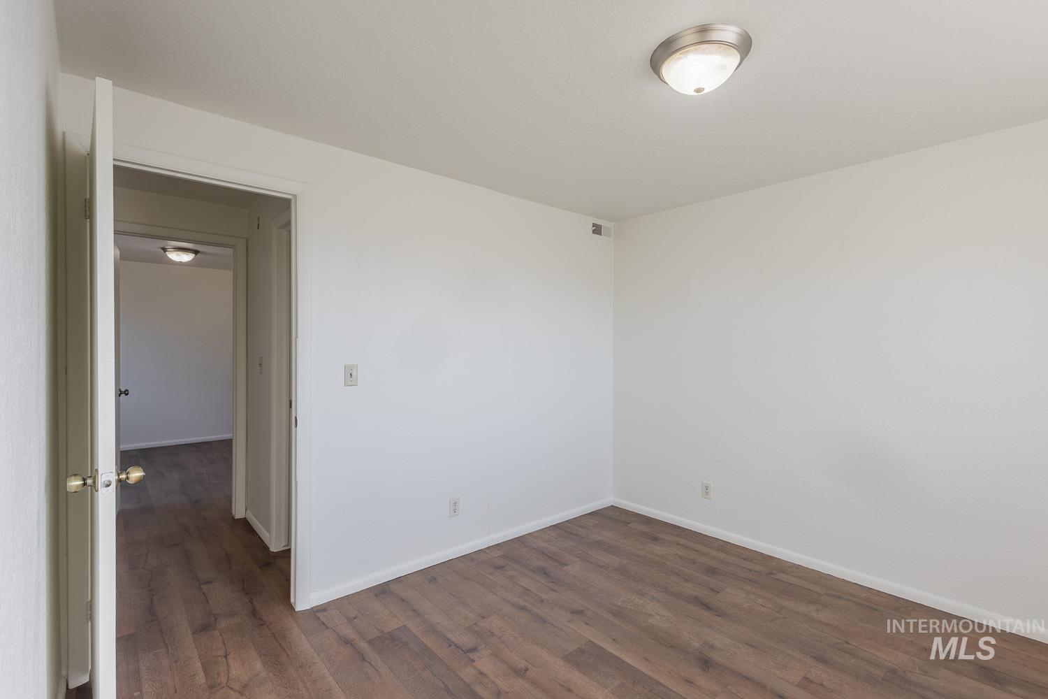 Spare room featuring dark wood-type flooring and baseboards