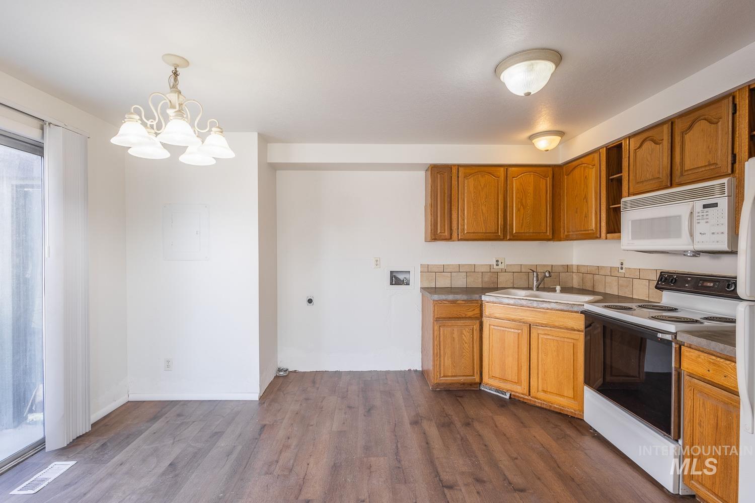 Kitchen featuring electric range oven, white microwave, a chandelier, brown cabinetry, and hanging light fixtures
