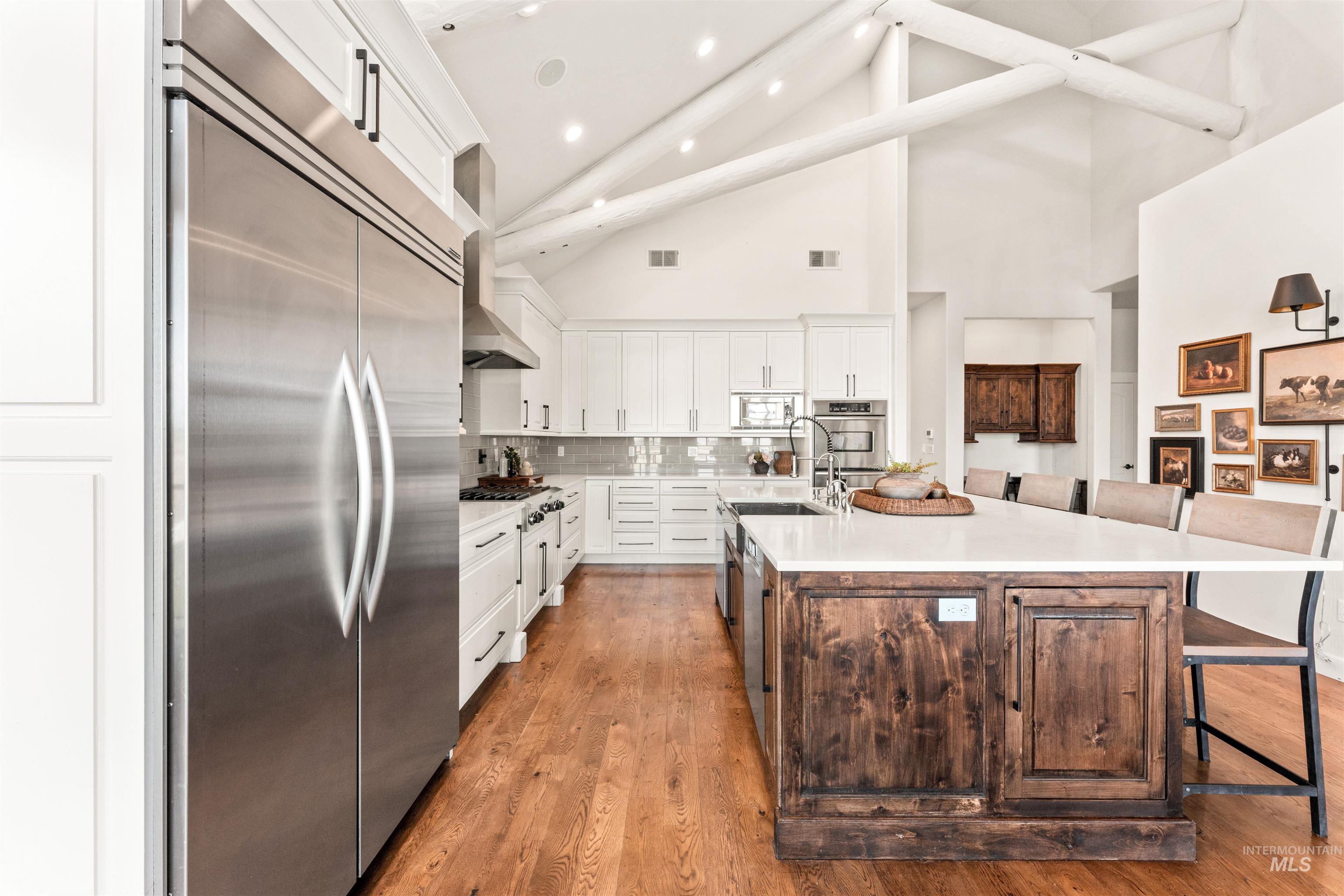 Kitchen with a kitchen breakfast bar, built in appliances, white cabinetry, high vaulted ceiling, and backsplash