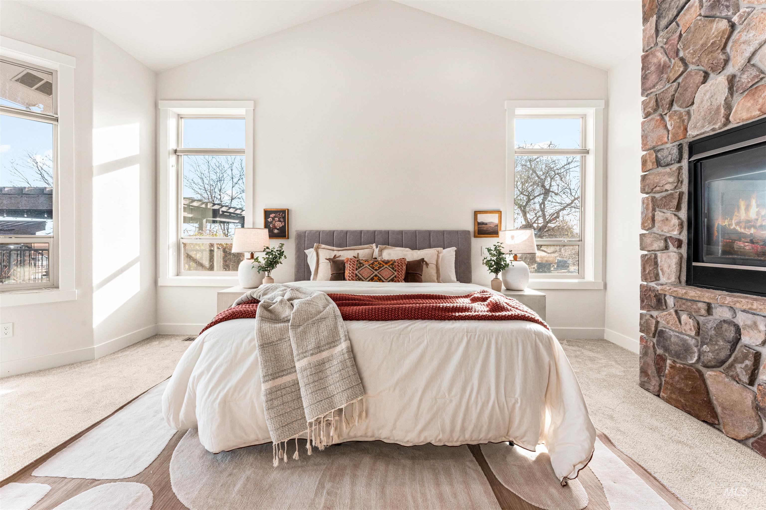 Carpeted bedroom with vaulted ceiling, a fireplace, and multiple windows