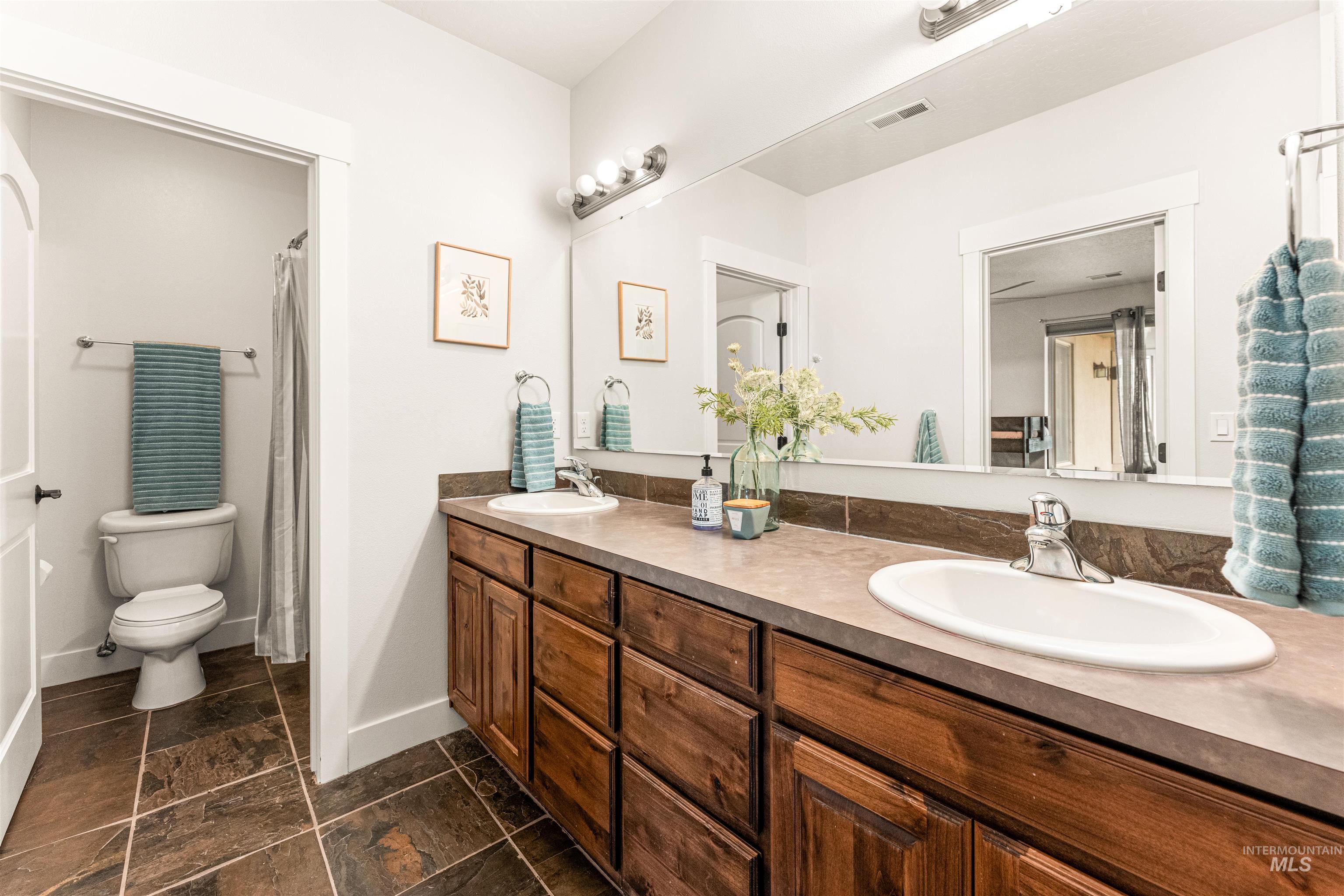 Bathroom featuring double vanity, a shower with shower curtain, and stone tile floors