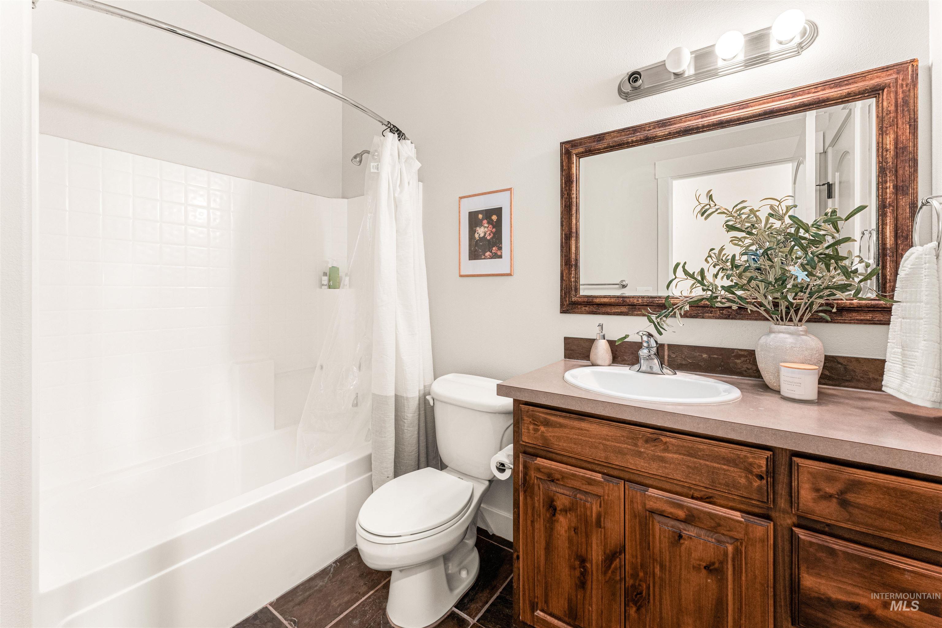 Bathroom featuring vanity, shower / bath combo, and dark tile patterned flooring