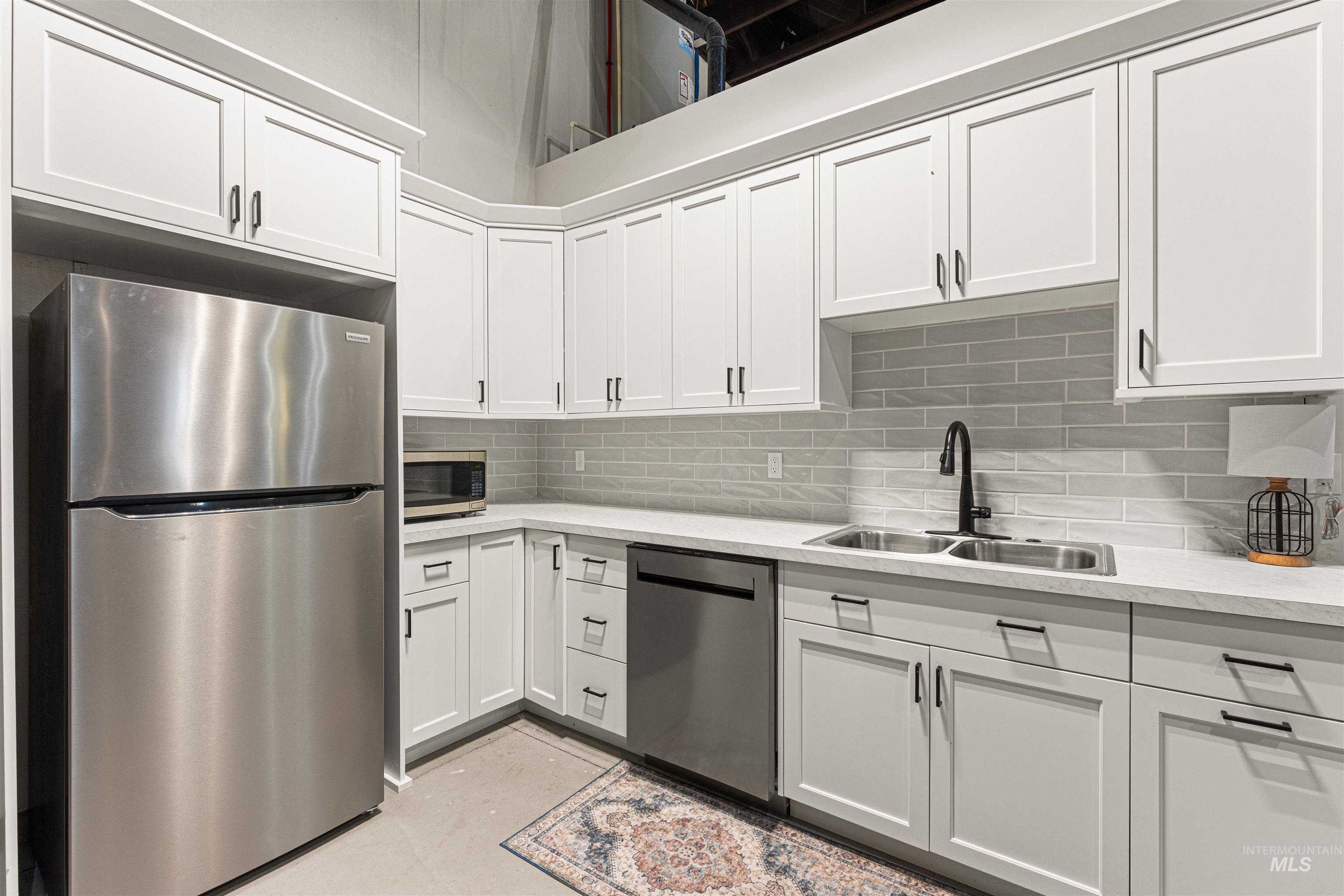Kitchen featuring stainless steel appliances, white cabinetry, tasteful backsplash, and light stone counters