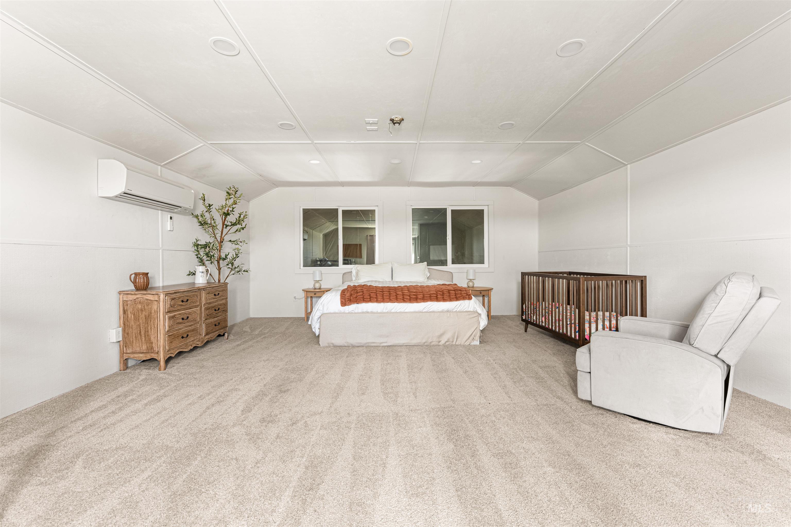 Bedroom featuring lofted ceiling, light colored carpet, and a wall mounted air conditioner
