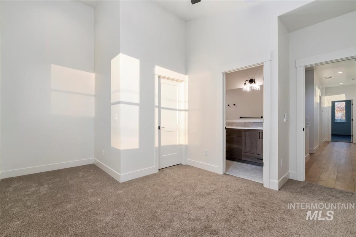 Unfurnished bedroom featuring light colored carpet, connected bathroom, and a towering ceiling