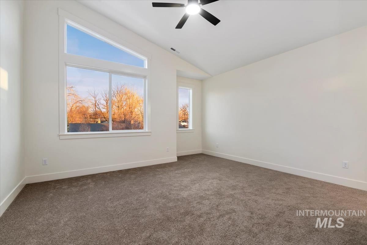 Carpeted empty room with lofted ceiling and a ceiling fan