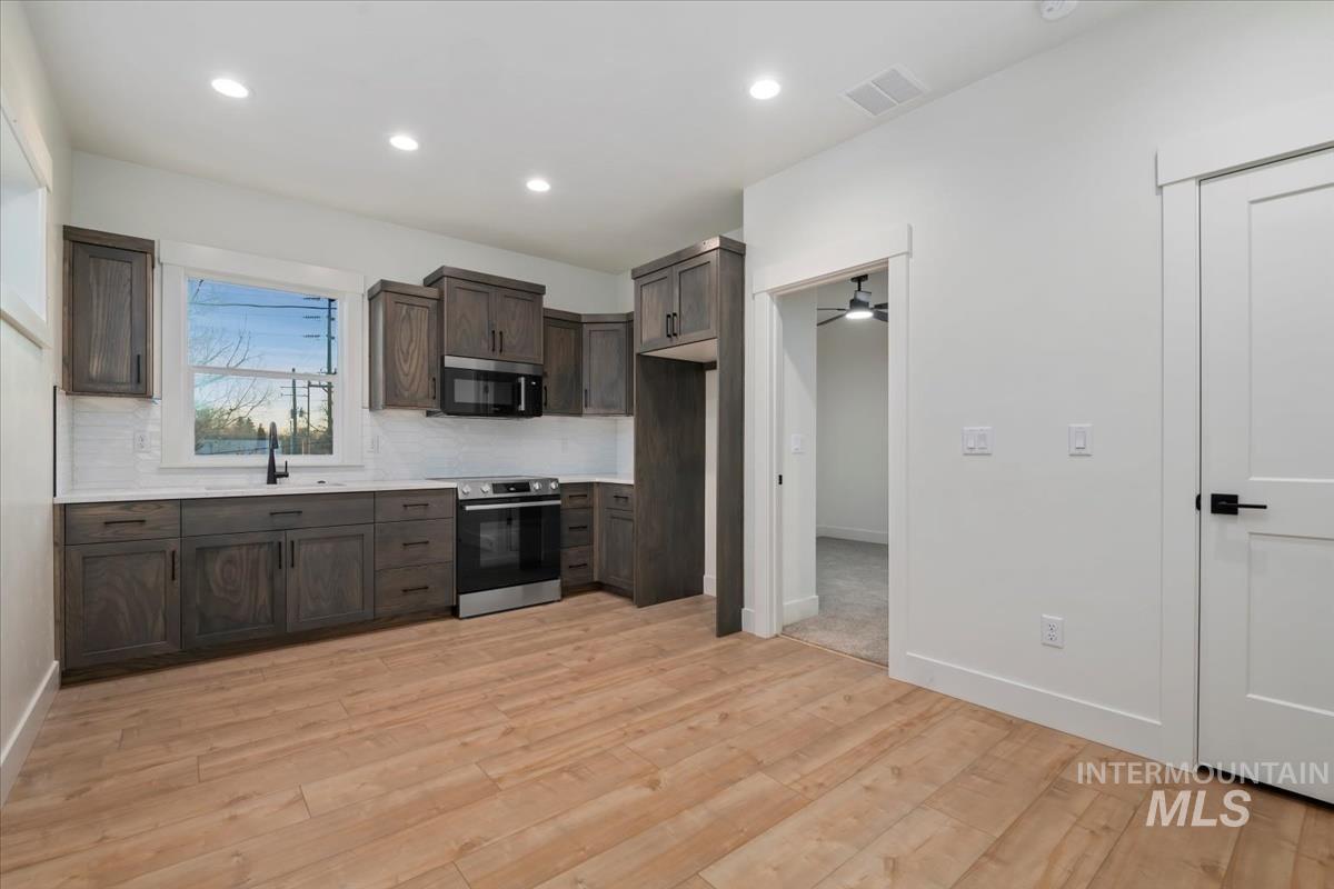 Kitchen with stainless steel appliances, light countertops, dark brown cabinetry, backsplash, and light wood finished floors