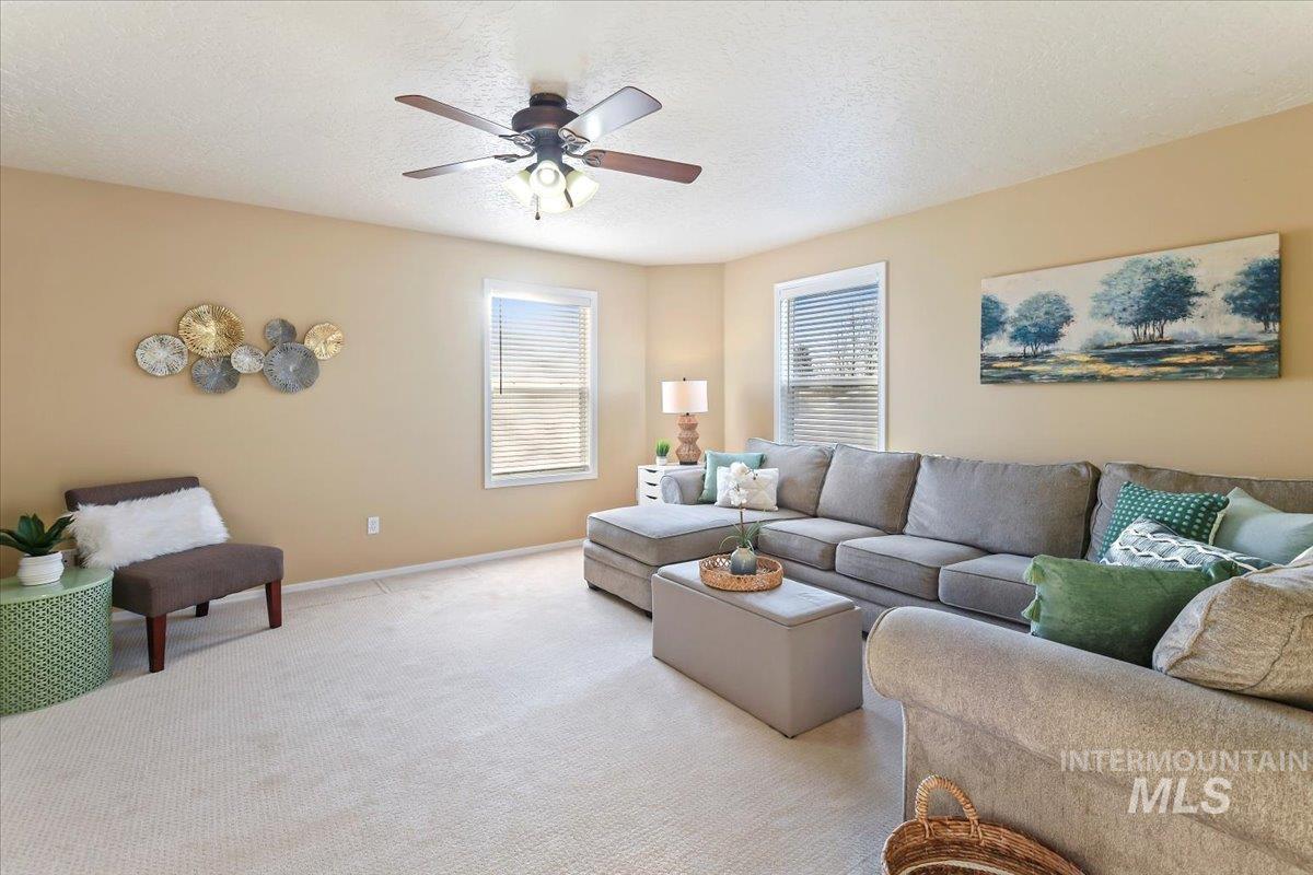 Living room with a textured ceiling, carpet floors, and a ceiling fan