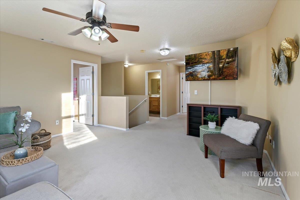 Sitting room featuring an upstairs landing, light colored carpet, a textured ceiling, and a ceiling fan